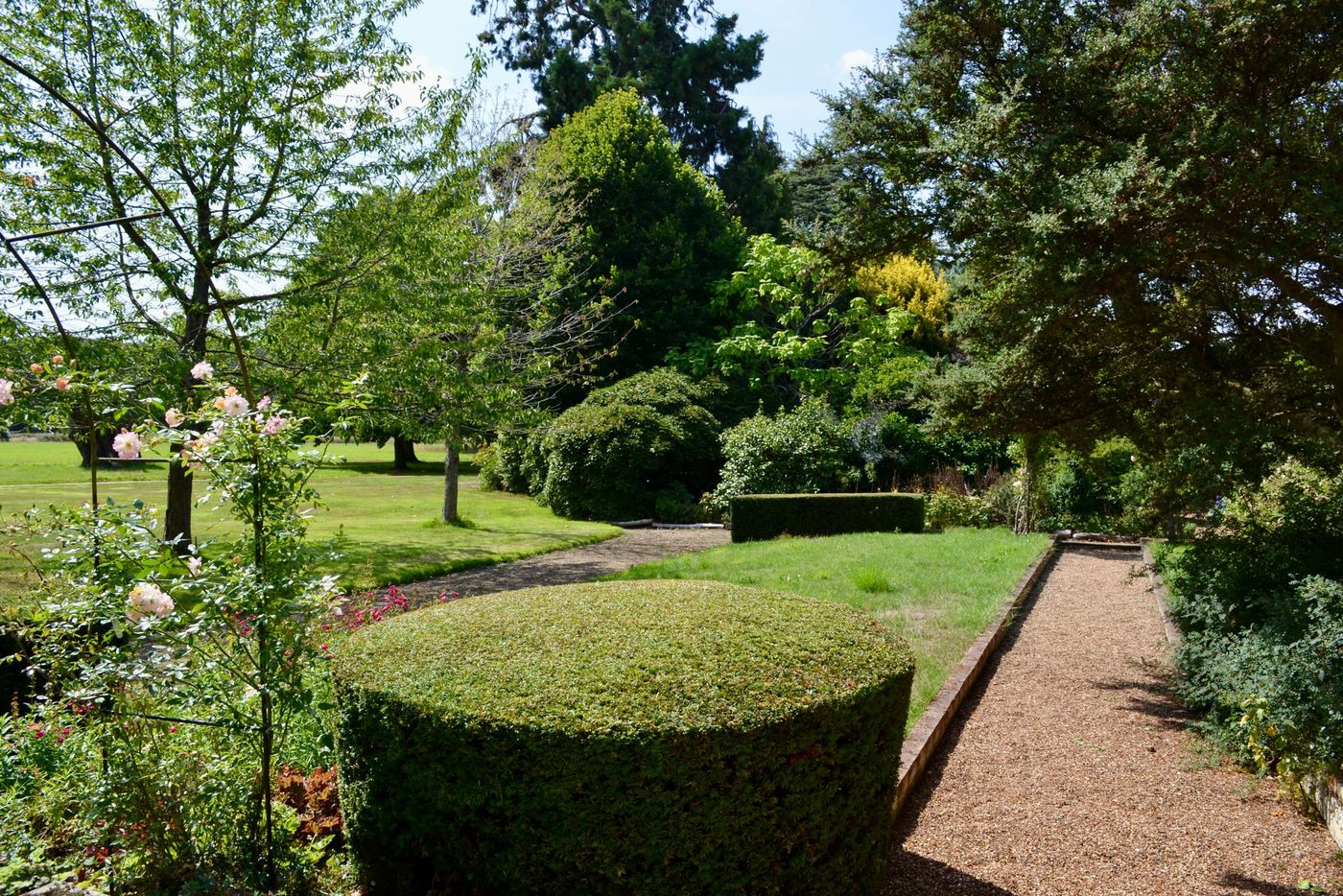 A well-kept garden with a clipped box hedge, gravel path and mature trees