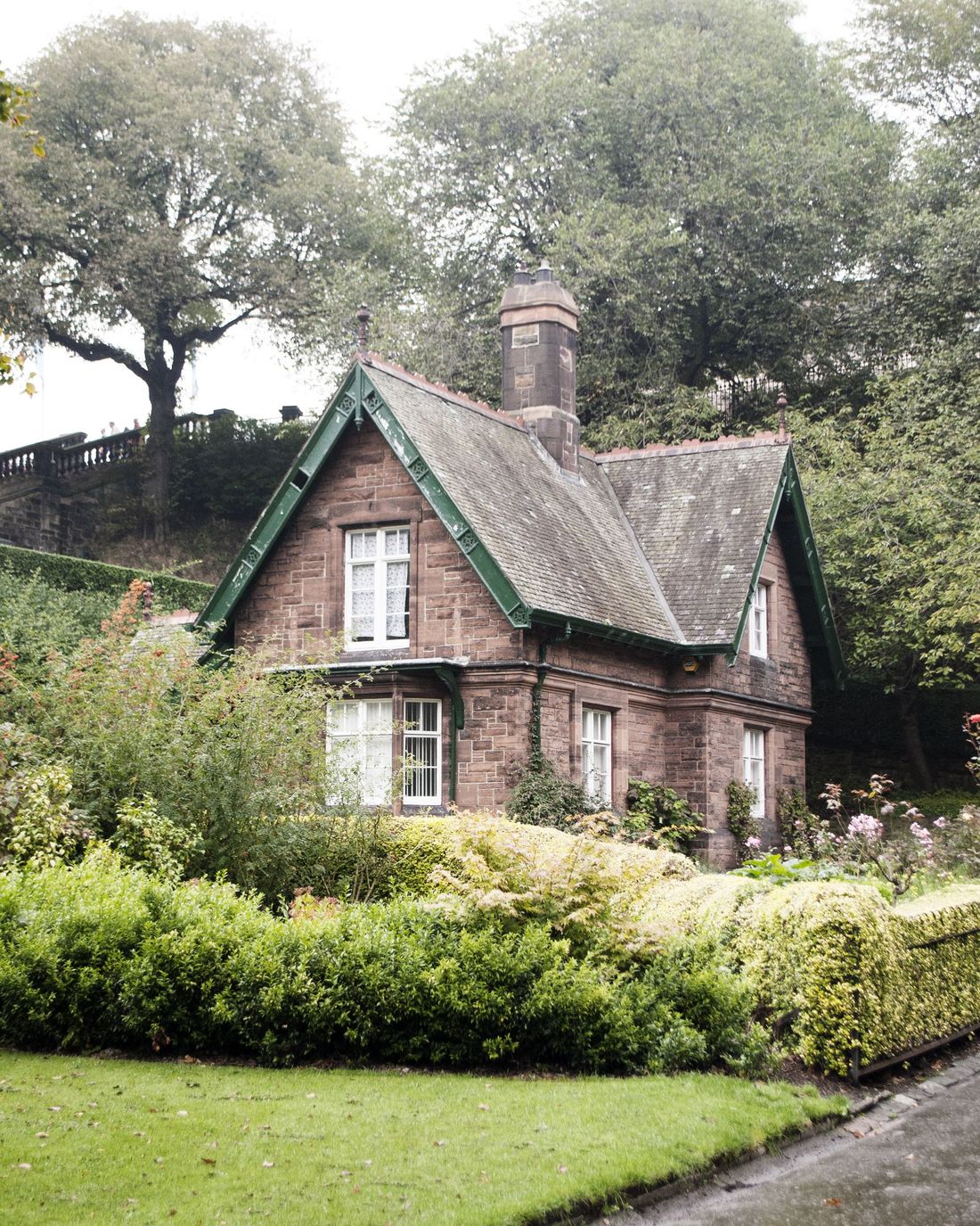 A brick cottage with a clipped shrub border and lawn beside a path